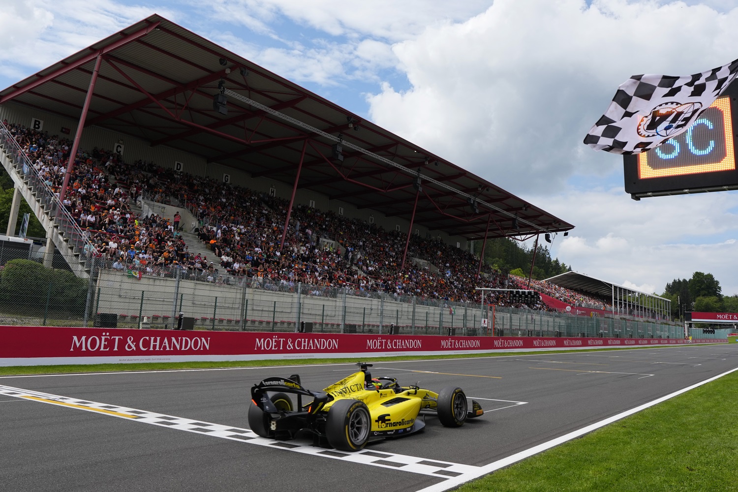 Leonardo Fornaroli au volant de sa monoplace jaune franchissant la ligne d'arrivée avec en arrière plan les tribunes.